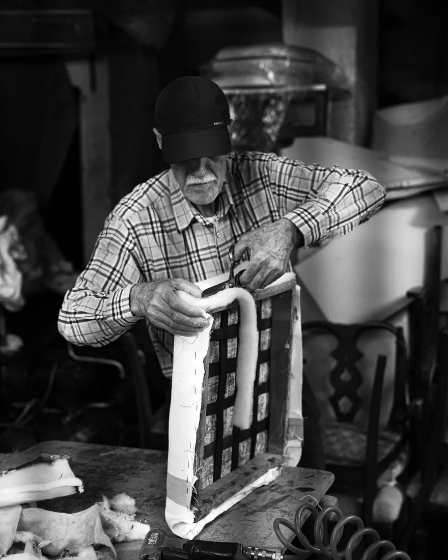 Artesano trabajando el tapizado de un asiento en un taller, con el material sujeto a mano